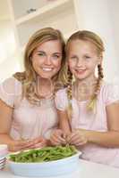 Young woman with child splitting pea in kitchen