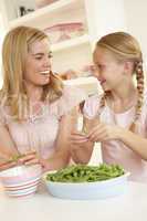 Young woman with child splitting pea in kitchen