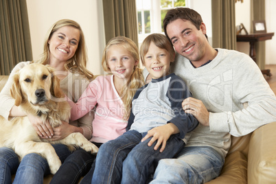 Happy young family sitting on sofa holding a dog