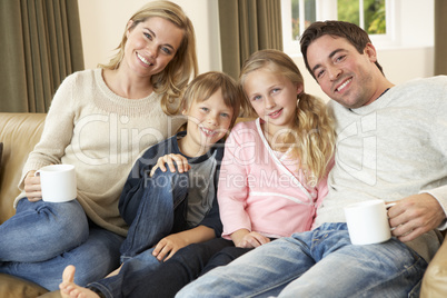 Happy young family sitting on sofa holding cups