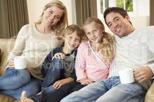 Happy young family sitting on sofa holding cups