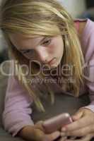 Unhappy Teenage Girl Lying In Bedroom With Mobile Phone