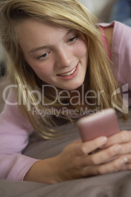 Teenage Girl Lying In Bedroom Using Mobile Phone
