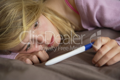 Depressed Teenage Girl Sitting In Bedroom With Pregnancy Test