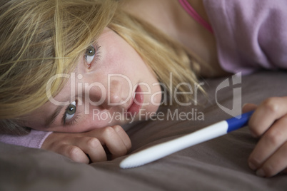 Depressed Teenage Girl Sitting In Bedroom With Pregnancy Test