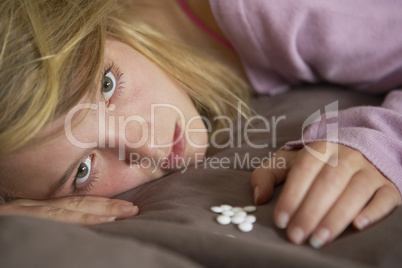 Depressed Teenage Girl Sitting In Bedroom With Pills