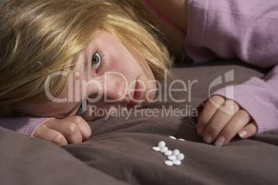 Depressed Teenage Girl Sitting In Bedroom With Pills