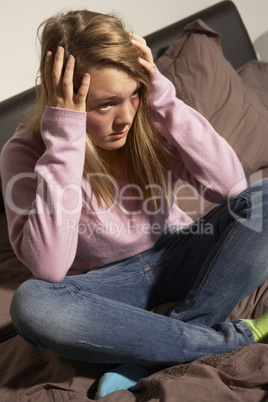 Depressed Teenage Girl Sitting In Bedroom At Home