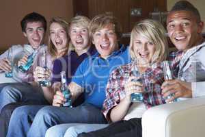 Group Of Teenage Friends Sitting On Sofa At Home Watching Drinki