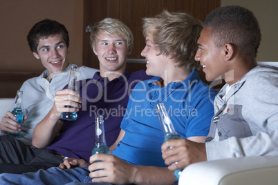 Group Of Teenage Boys Sitting On Sofa At Home Watching Drinking