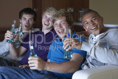 Group Of Teenage Boys Sitting On Sofa At Home Watching Drinking