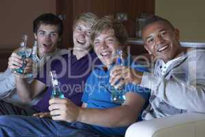 Group Of Teenage Boys Sitting On Sofa At Home Watching Drinking