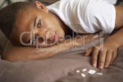 Depressed Teenage Boy Lying In Bedroom With Pills