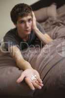 Depressed Teenage Boy Sitting In Bedroom With Pills