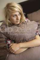 Depressed Teenage Girl Hugging Pillow In Bedroom
