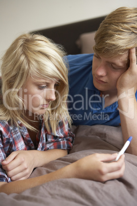 Two Teenage Girls Lying On Bed Looking At Pregnancy Testing Kit