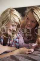 Two Teenage Girls Lying On Bed With Mobile Phone