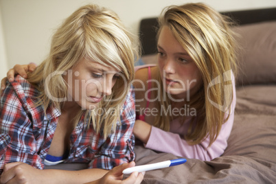 Two Teenage Girls Lying On Bed Looking At Pregnancy Testing Kit