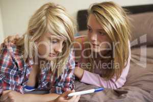 Two Teenage Girls Lying On Bed Looking At Pregnancy Testing Kit