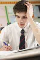 Stressed Male Teenage Student Studying In Classroom