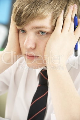 Stressed Male Teenage Student Studying In Classroom