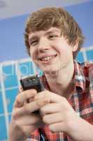 Male Teenage Student Using Mobile Phone By Lockers In School