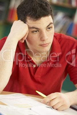 Stressed Male Teenage Student Studying In Classroom