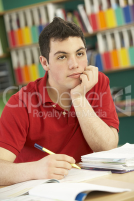 Stressed Male Teenage Student Studying In Classroom