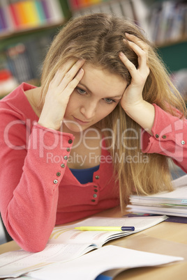 Stressed Female Teenage Student Studying In Classroom