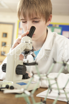 Male Teenage Student In Science Class Looking Through Microscope