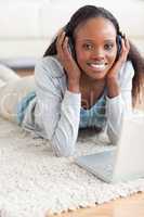 Close up of woman lying on the floor with her laptop listening t