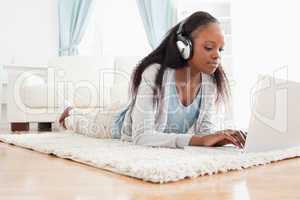 Woman lying on the floor with her laptop listening to music