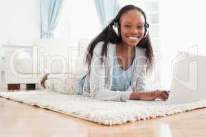 Woman lying on the floor with her notebook listening to music