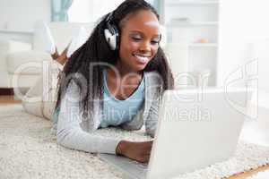 Woman lying on floor with her notebook listening to music