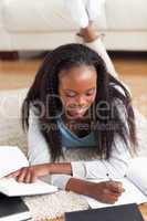 Woman lying on carpet in living room doing homework