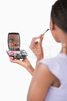 Close up of shadowing woman while applying make-up against a whi