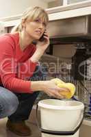 Woman Mopping Up Leaking Sink On Phone To Plumber