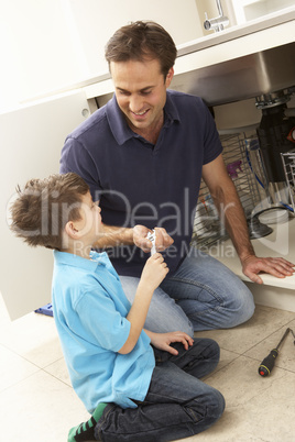 Son Helping Father To Mend Sink In Kitchen