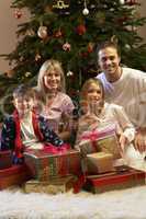 Family Opening Christmas Present In Front Of Tree