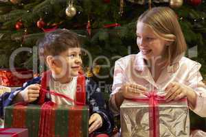 Children Opening Christmas Present In Front Of Tree