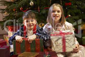 Children Opening Christmas Present In Front Of Tree