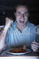 Man Enjoying Meal And Cheering Whilst Watching TV