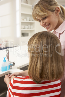 Mother And Daughter Washing Hands At Kitchen Sink