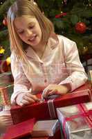 Young Girl Opening Christmas Present In Front Of Tree