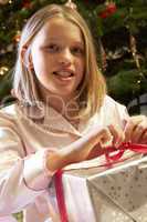 Young Girl Opening Christmas Present In Front Of Tree