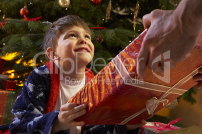 Young Boy Receiving Christmas Present In Front Of Tree
