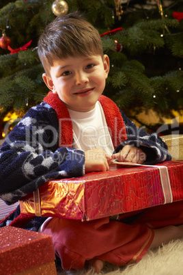 Young Boy Opening Christmas Present In Front Of Tree