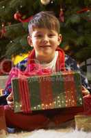 Young Boy Opening Christmas Present In Front Of Tree