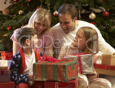 Family Opening Christmas Present In Front Of Tree