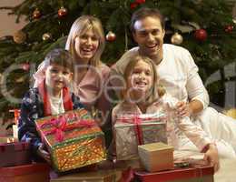 Family Opening Christmas Present In Front Of Tree